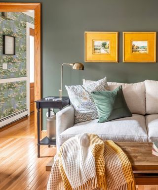 A dark green living room with framed artwork and a gray couch
