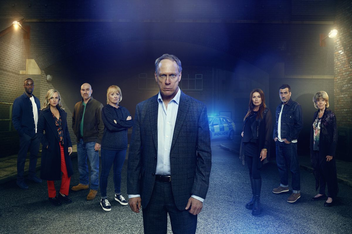 Stephen Reid stands in the centre with the Coronation Street residents around him and a police car in the background.