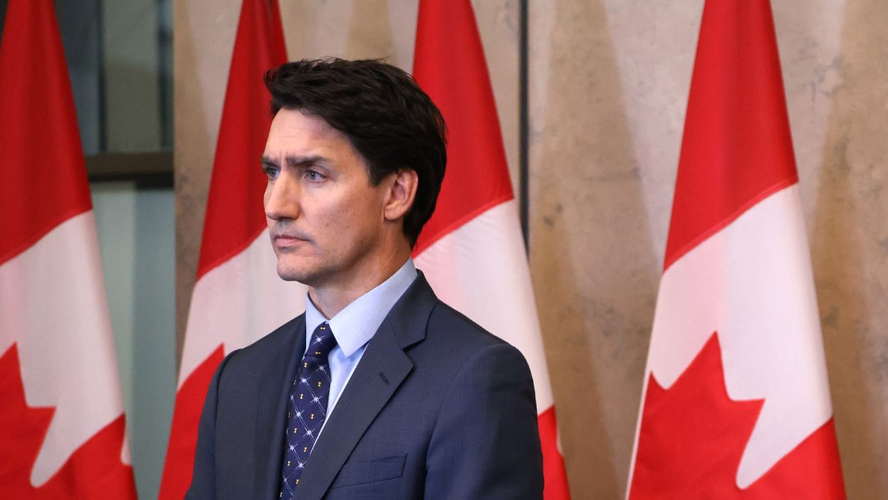 Canadian prime minister Justin Trudeau stands in front of Canadian flag, frowning