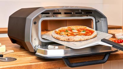 The Ooni Volt 12 (an indoor and outdoor pizza oven) in a kitchen, being used to cook a pizza 