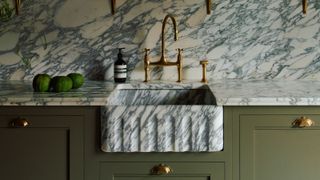 A marble sink with a veined marble kitchen backsplash and olive green cabinetry 