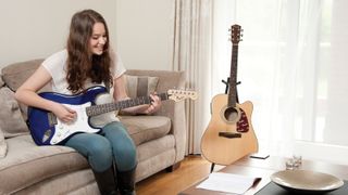 Woman plays Squier guitar with Fender acoustic in the background