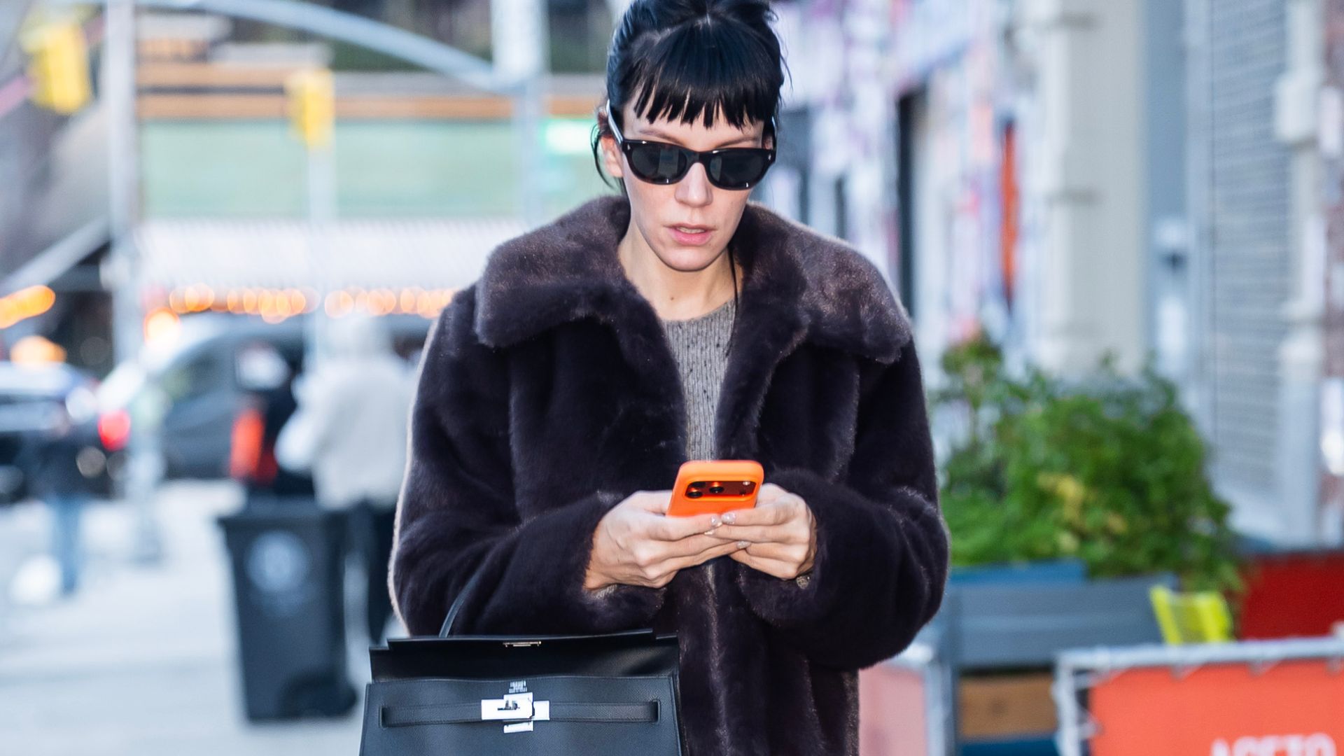 Lily Allen wears Hush fur jacket with a grey jumper a black leather skirt black lug-sole boots and a black Hermes bag and black sunglasses.