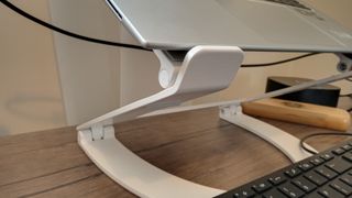 A white z-type Curve Flex laptop stand on a brown desk