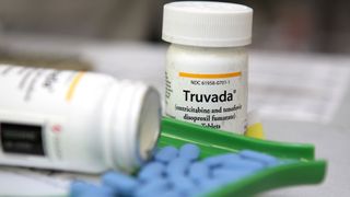 photo of a closed bottle of truvada (an hiv medication) sitting next to an open bottle with blue pills being weighed out next to it
