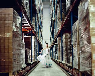 A female in a white flamenco dress stood between tall warehouse shelves