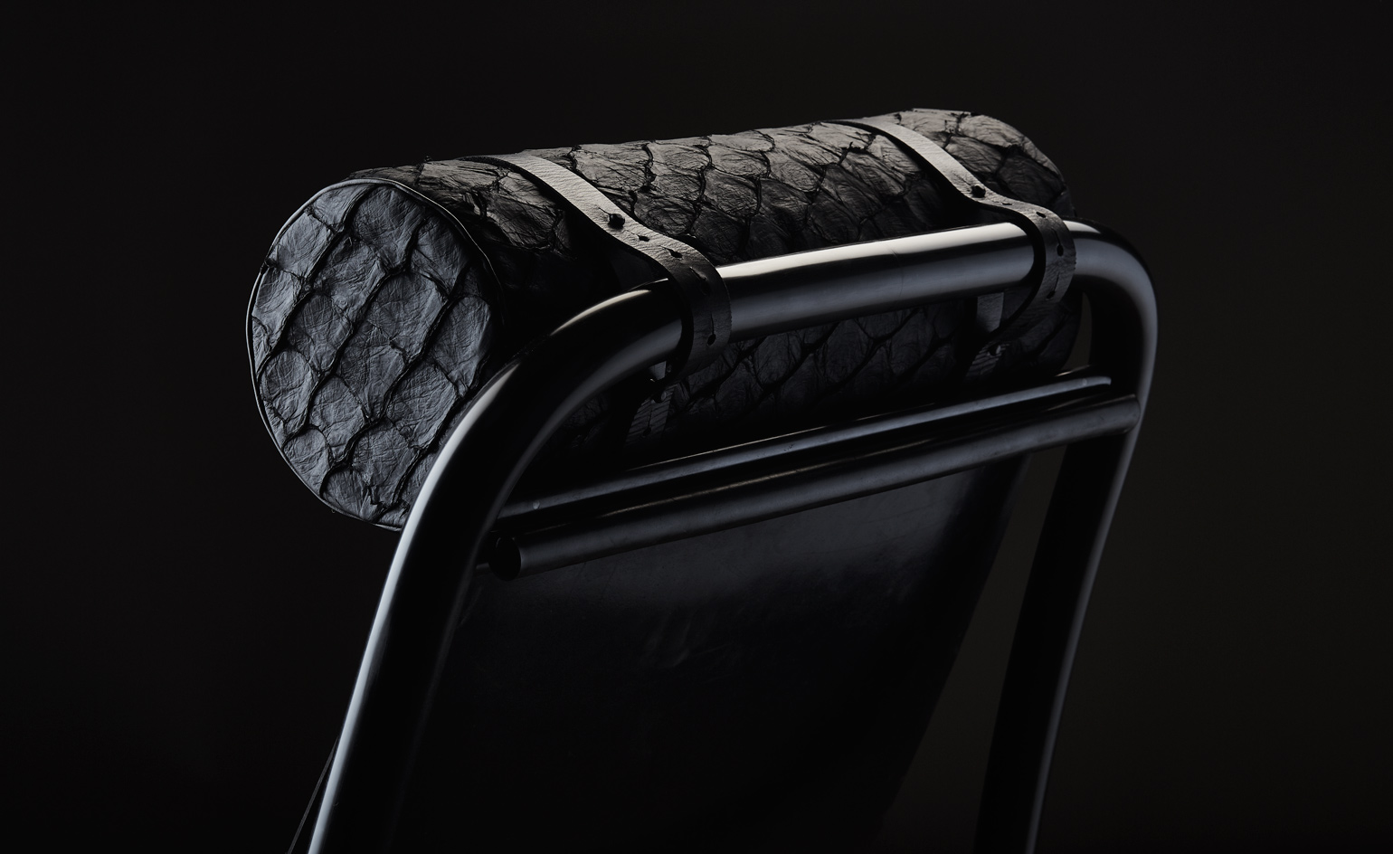 Close up view of a black chair by Studio Swine featuring a fish skin covered bolster cushion at the top