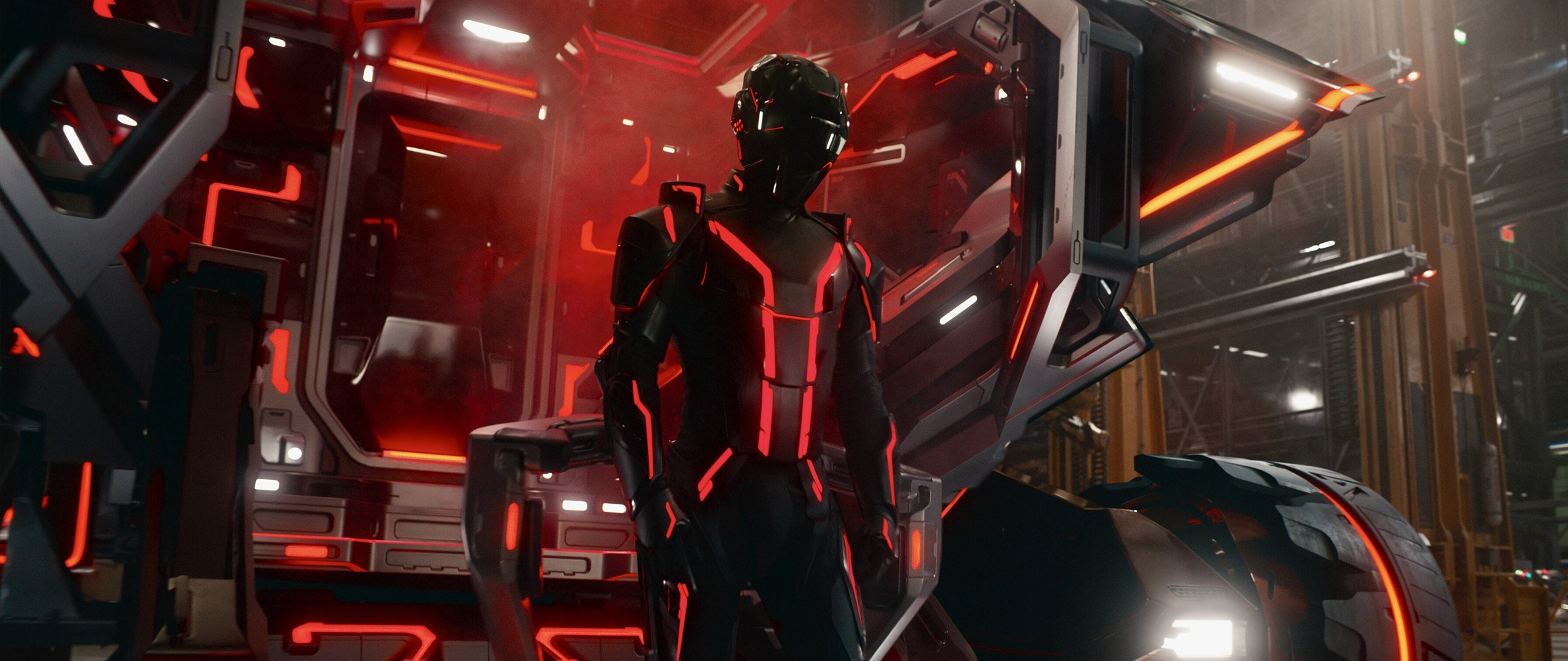 A person wearing a Tron suit stands in front of a vehicle in a warehouse