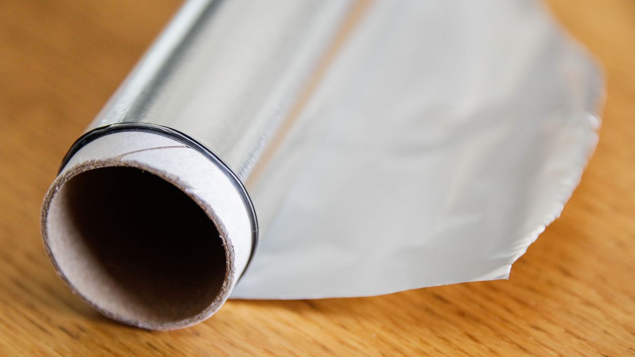 Opened roll of aluminum foil on a wooden counter, for article about cleaning with alumunium foil entitled &#039;10 ways to clean with aluminum foil&#039;