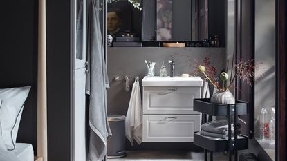 A dark grey small ensuite bathroom with a wash stand in light grey and black, with white sink basin and vanity