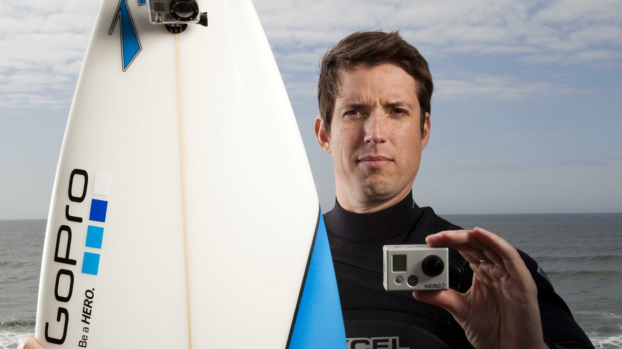 GoPro CEO Nick Woodman holding up a GoPro Hero 2 camera on a beach