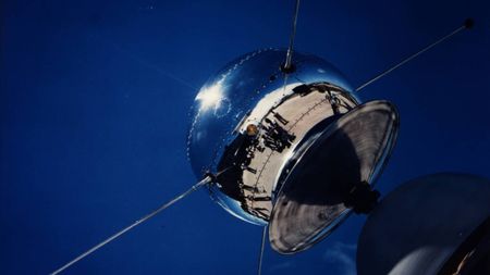 a silver, metallic orb on the tip of a rounded rocket nose cone, seen against a blue sky