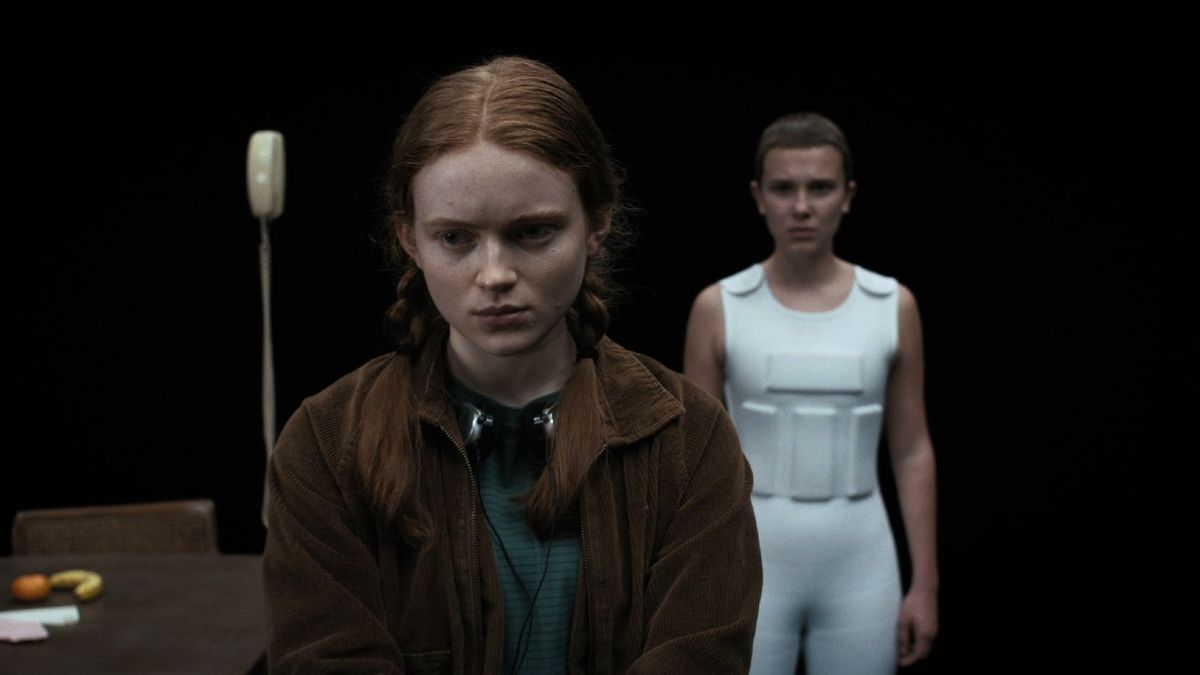 From left to right: Sadie Sink looking down as Max with Millie Bobby Brown standing behind her as Eleven. They&#039;re standing in a dark void.