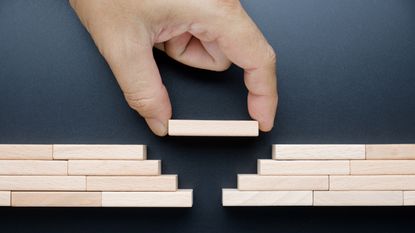 A man puts a block over a gap between other blocks, only his fingers showing.