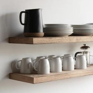 Mugs and small jugs lined up in the same direction on a wooden floating shelf