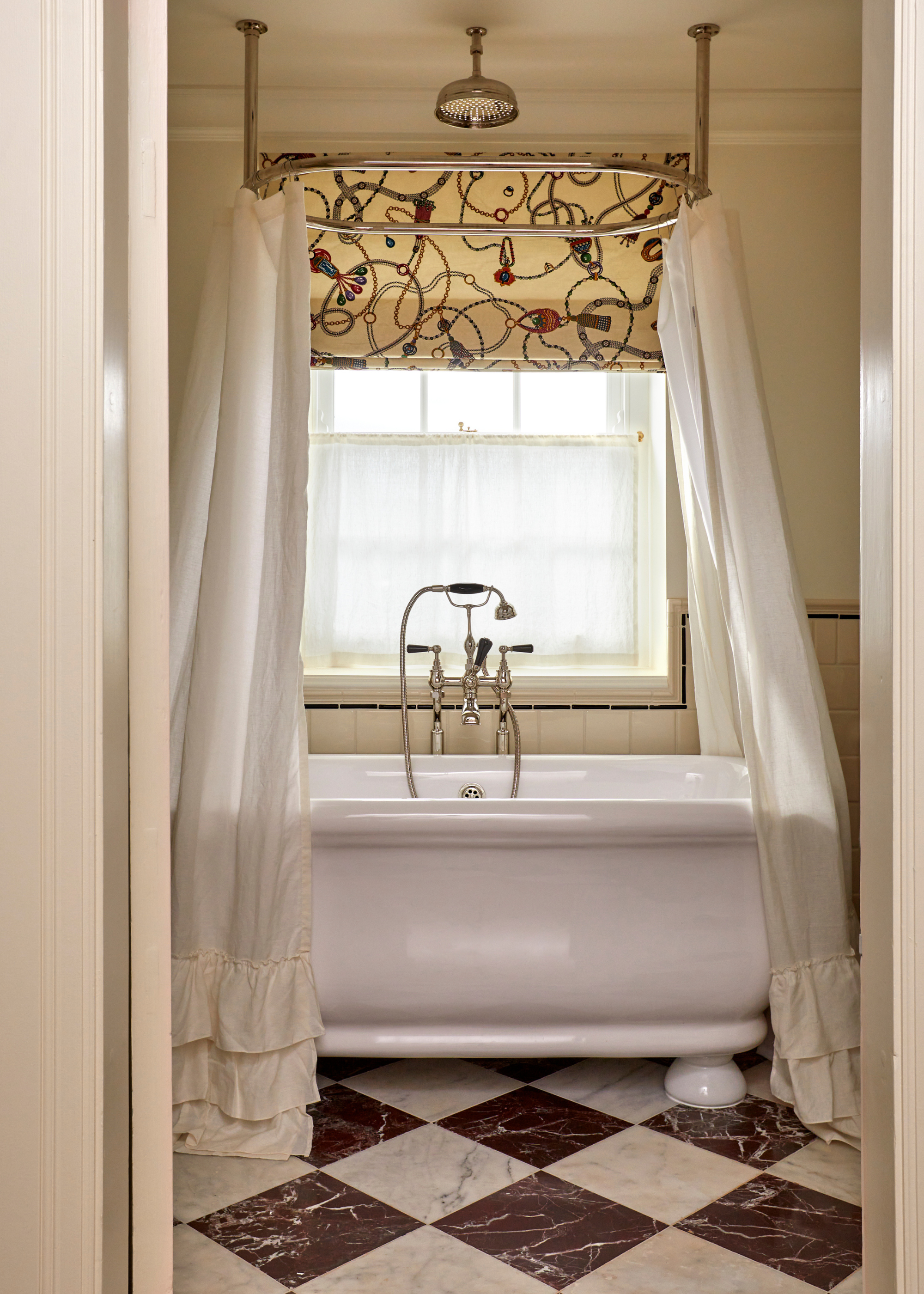 a checkerboard tiled bathroom with a white freestanding bath and a ruffled shower curtain