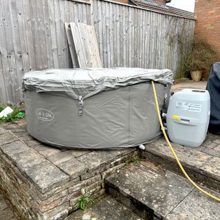 The grey inflatable Lay-Z-Spa Barbados hot tub outside on a patio with a yellow hosepipe held under the lid