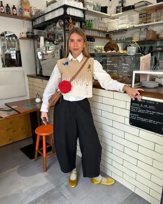 a woman wears a sweater vest with black trousers