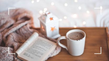 a book and hot drink with candle on a table—to illustrate the best books to gift loved ones this Christmas