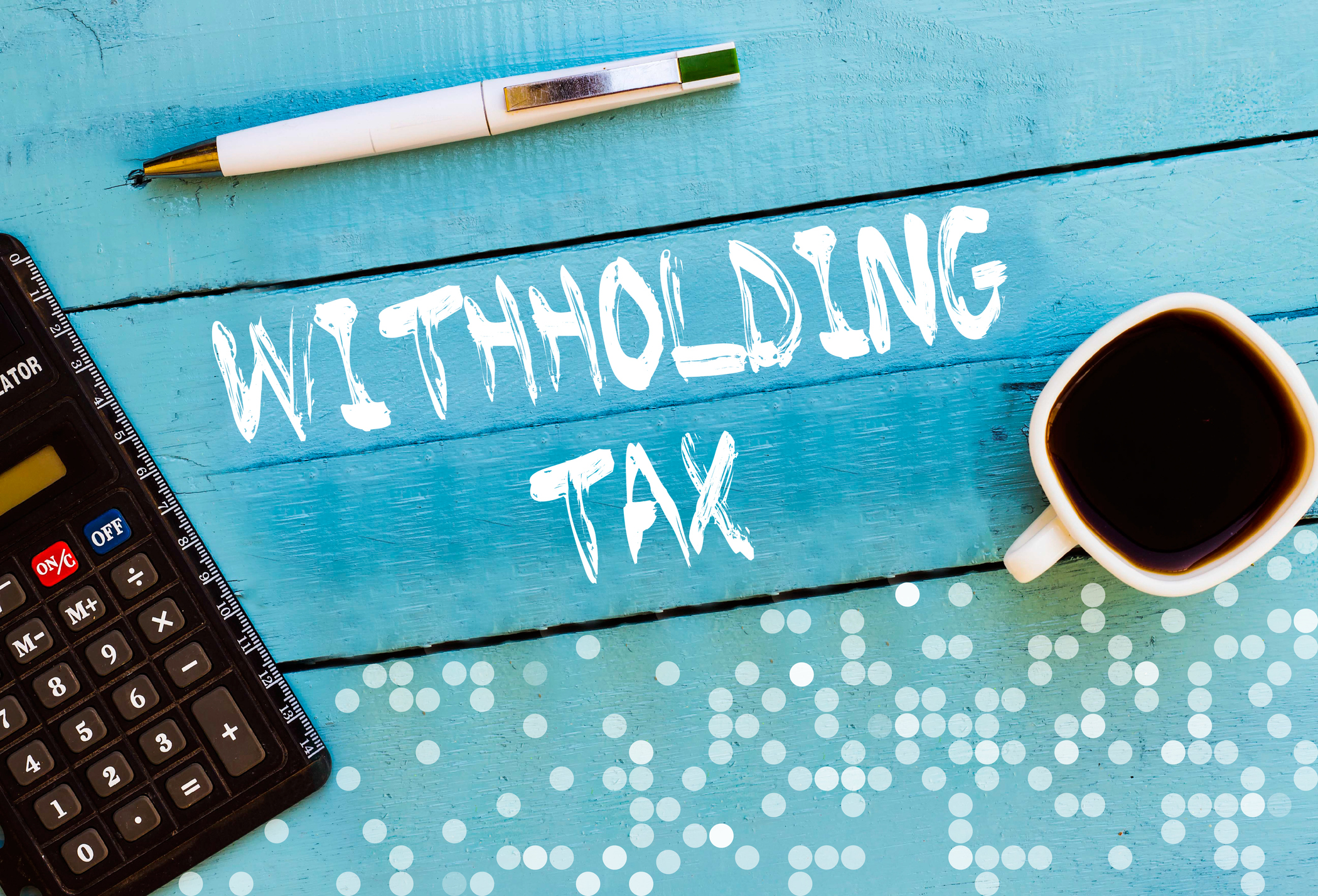 "Withholding tax" written on a blue table with a pen, calculator, and coffee cup