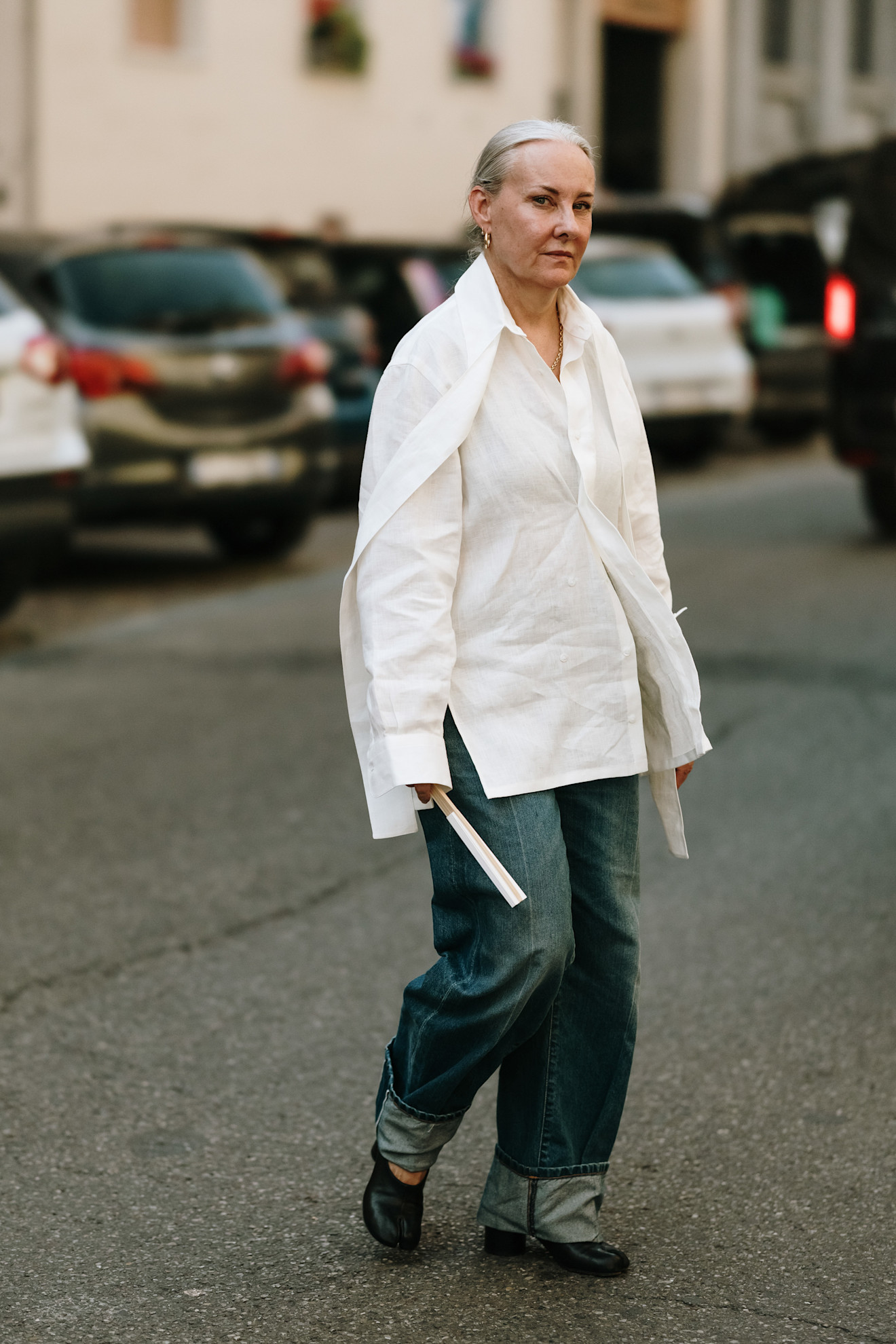 a woman at milan fashion week wearing medium-wash cuffed jeans with black Tabi flats and a white button-down shirt