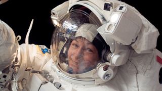 peggy whitson in a spacesuit smiling during a spacewalk. black space is behind her