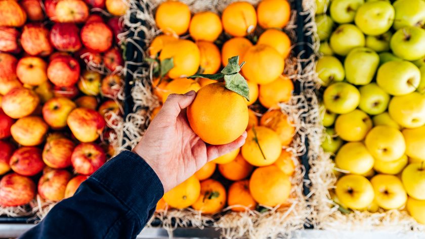 a hand holding an orange over baskets of fruit
