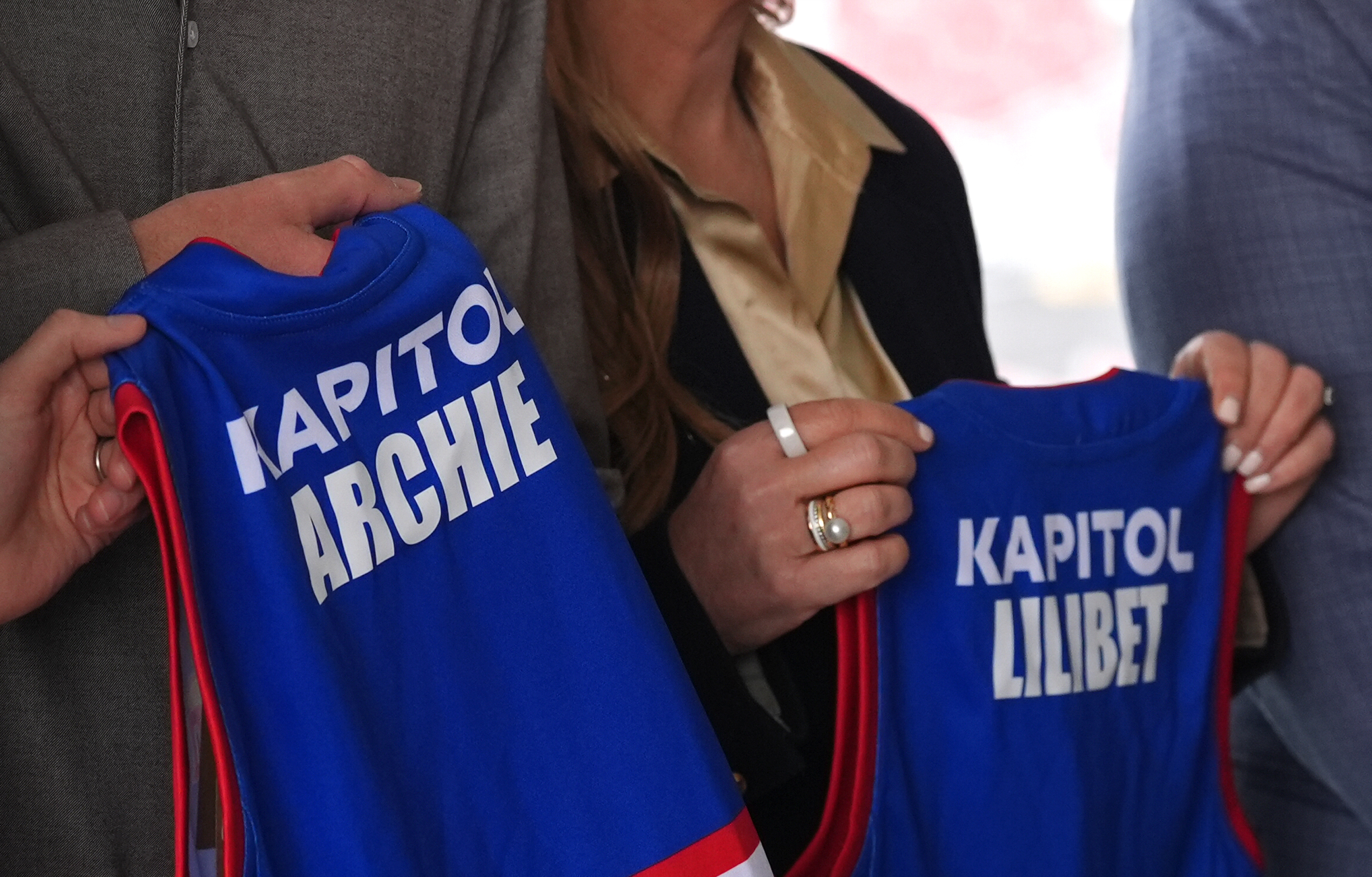 Prince Harry holding jerseys that say Prince Archie and Princess Lilbet
