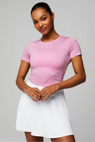 a model wears a short-sleeve pink T-shirt with a white skirt