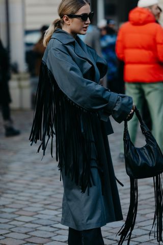 A woman in a blue fringe coat and jeans standing in the street at Copenhagen