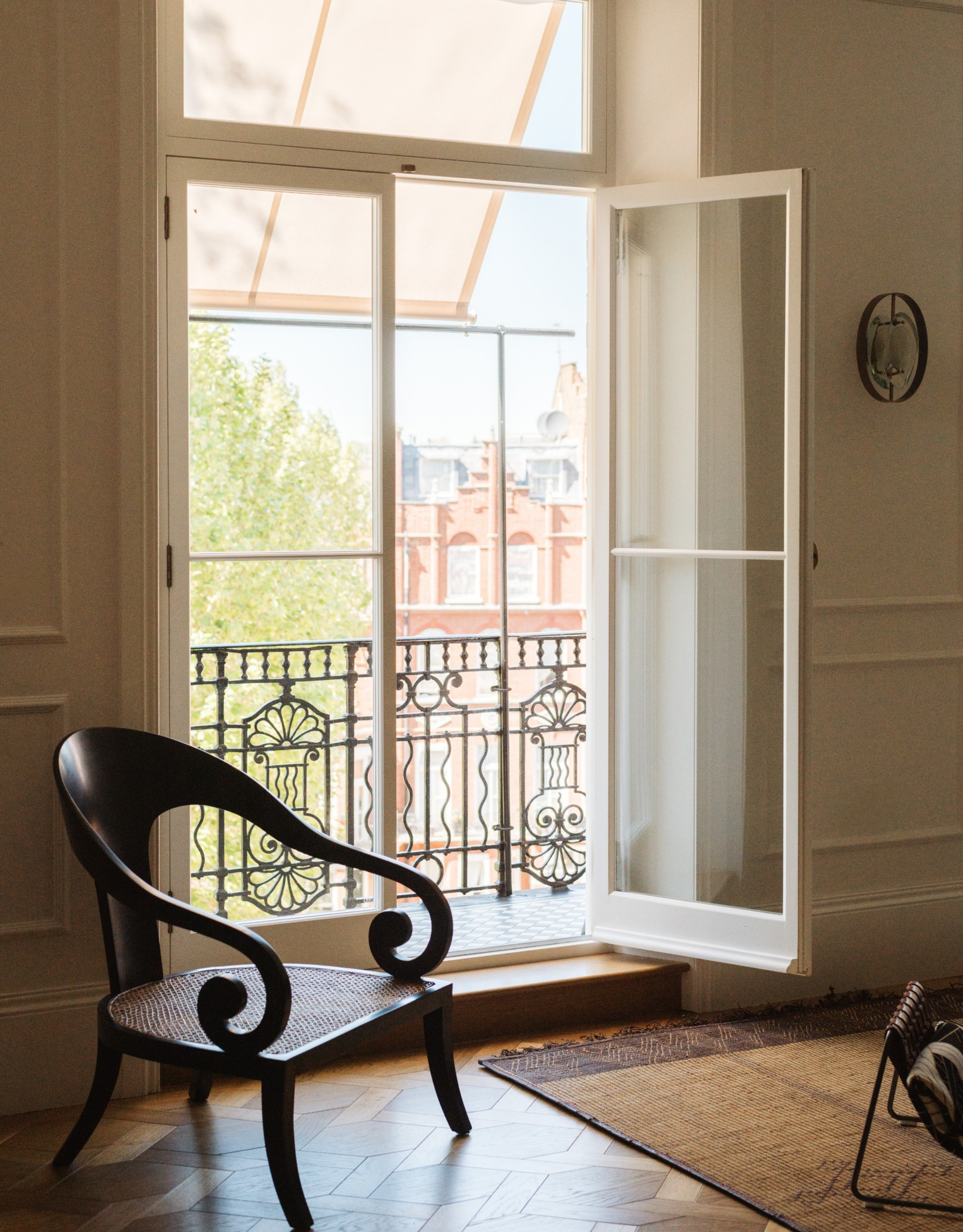 large floor-to-ceiling window with open doors and a vintage wooden armchair in front of the window