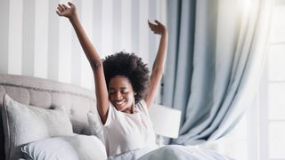 A woman wakes up and stretches on her bed in a bedroom