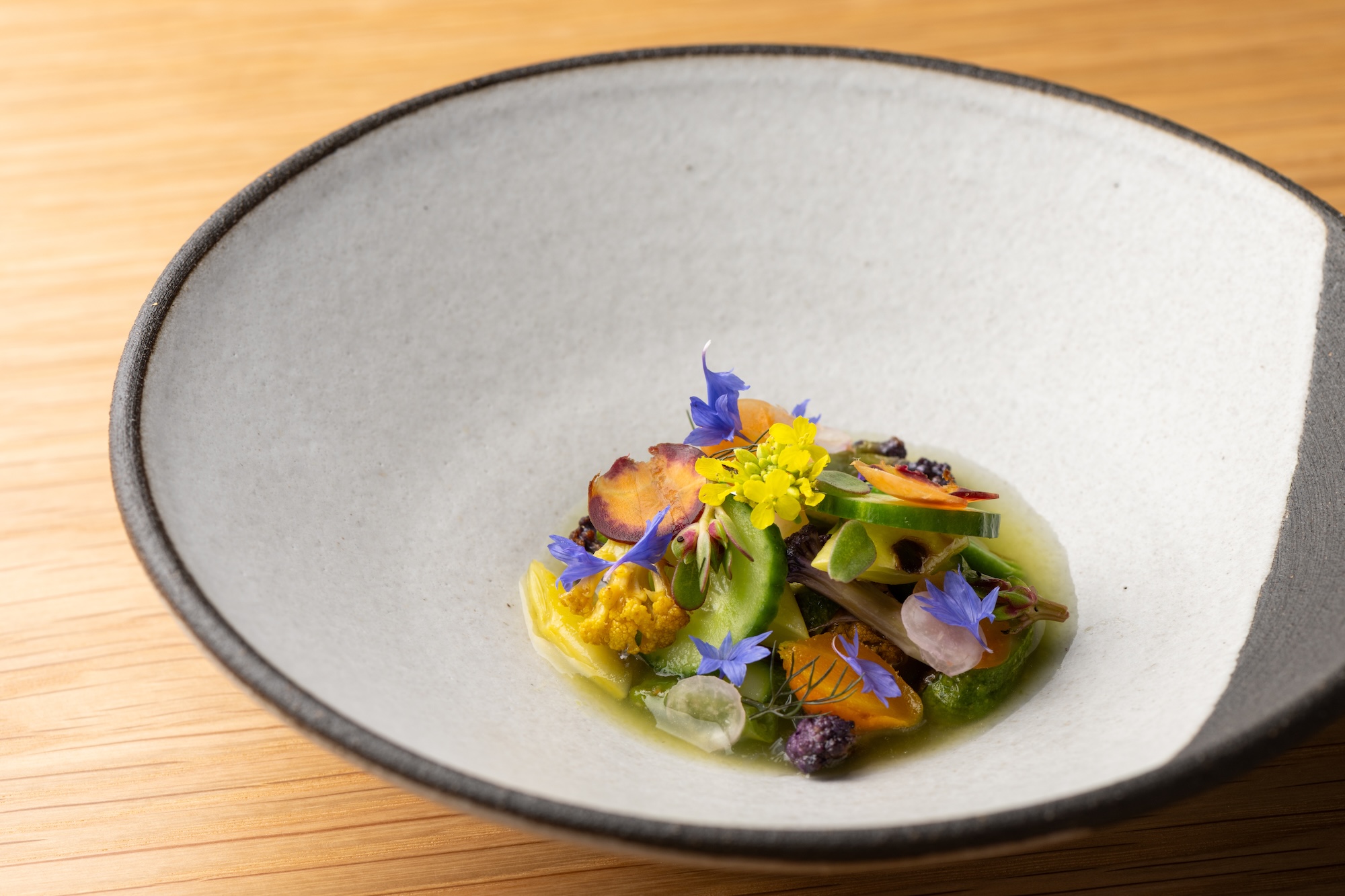 a dish from jacaranda los angeles with a green broth and flowers