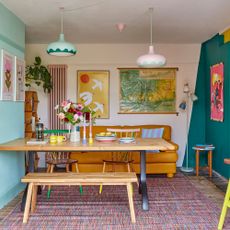 Colourful dining area with wooden table and bench and mustard yellow sofa