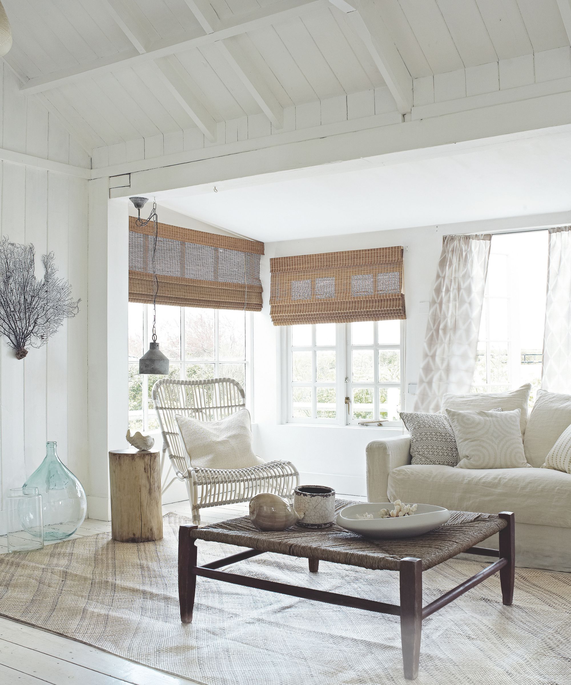 Neutral living room with white panelled ceiling, white linen sofa, wood coffee table and wicker chair