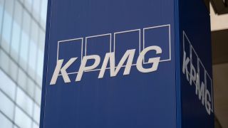 KMPG logo (the white letters "KPMG" against four white rectangles with blue centers) on a blue pillar outside the KPMG office.