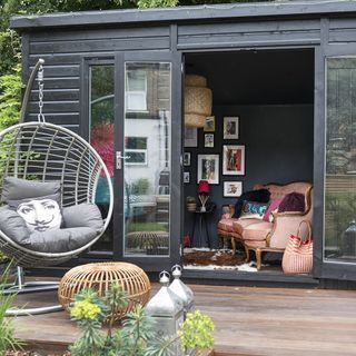 garden room with black wooden walls and sofa set with cushions