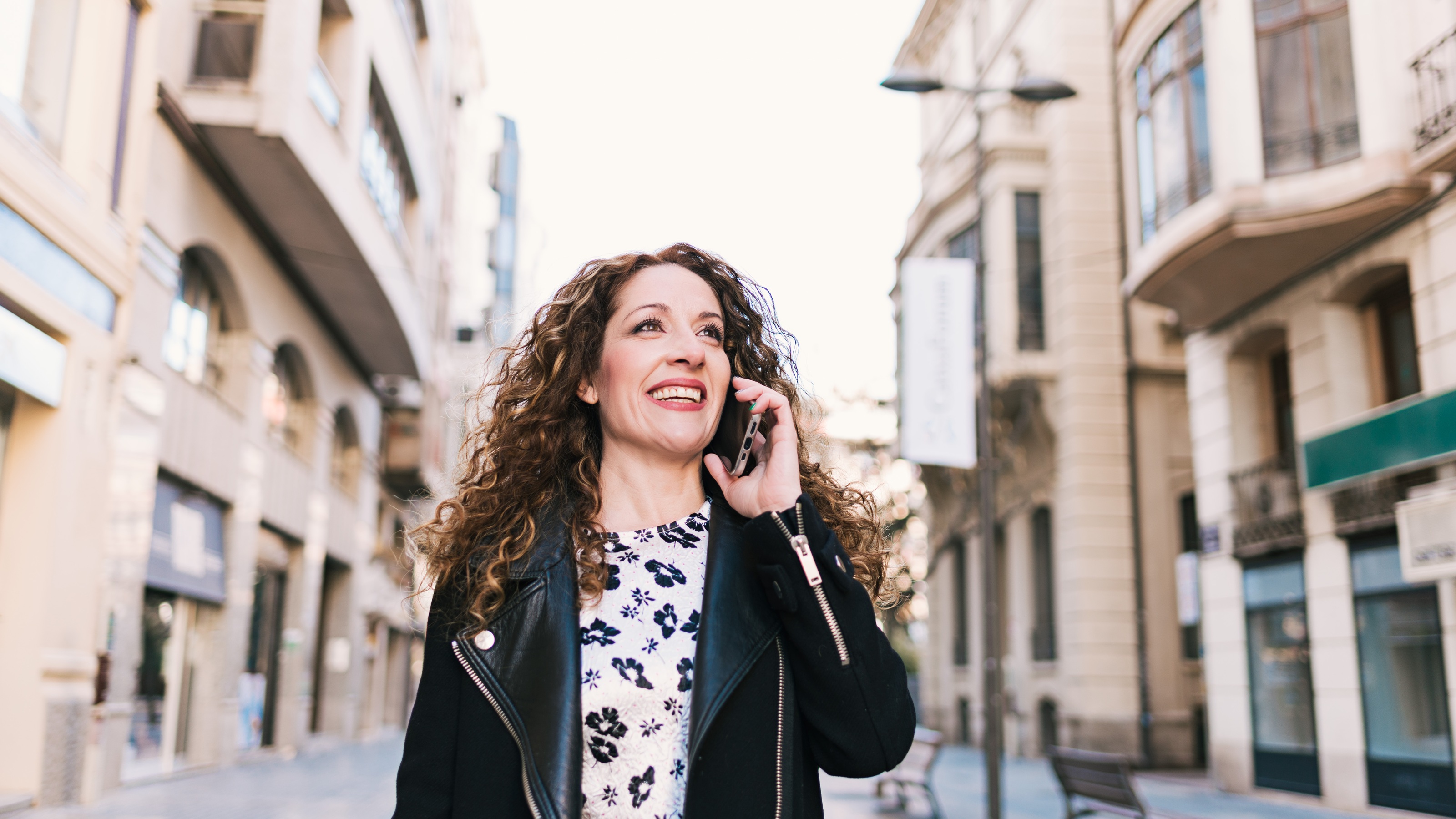 A woman talks on her phone as she walks through a street in Spain.