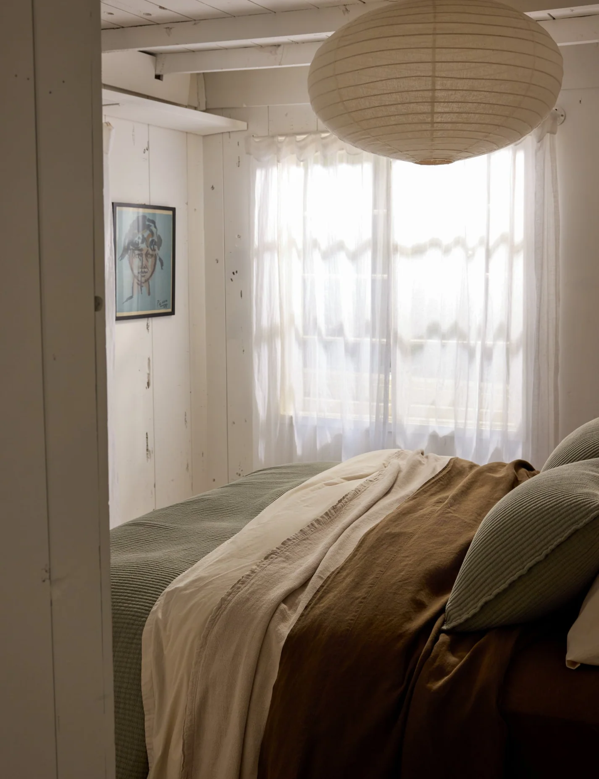 Moss green bed sheets pictured in beachy bedroom accented with a lantern pendant light