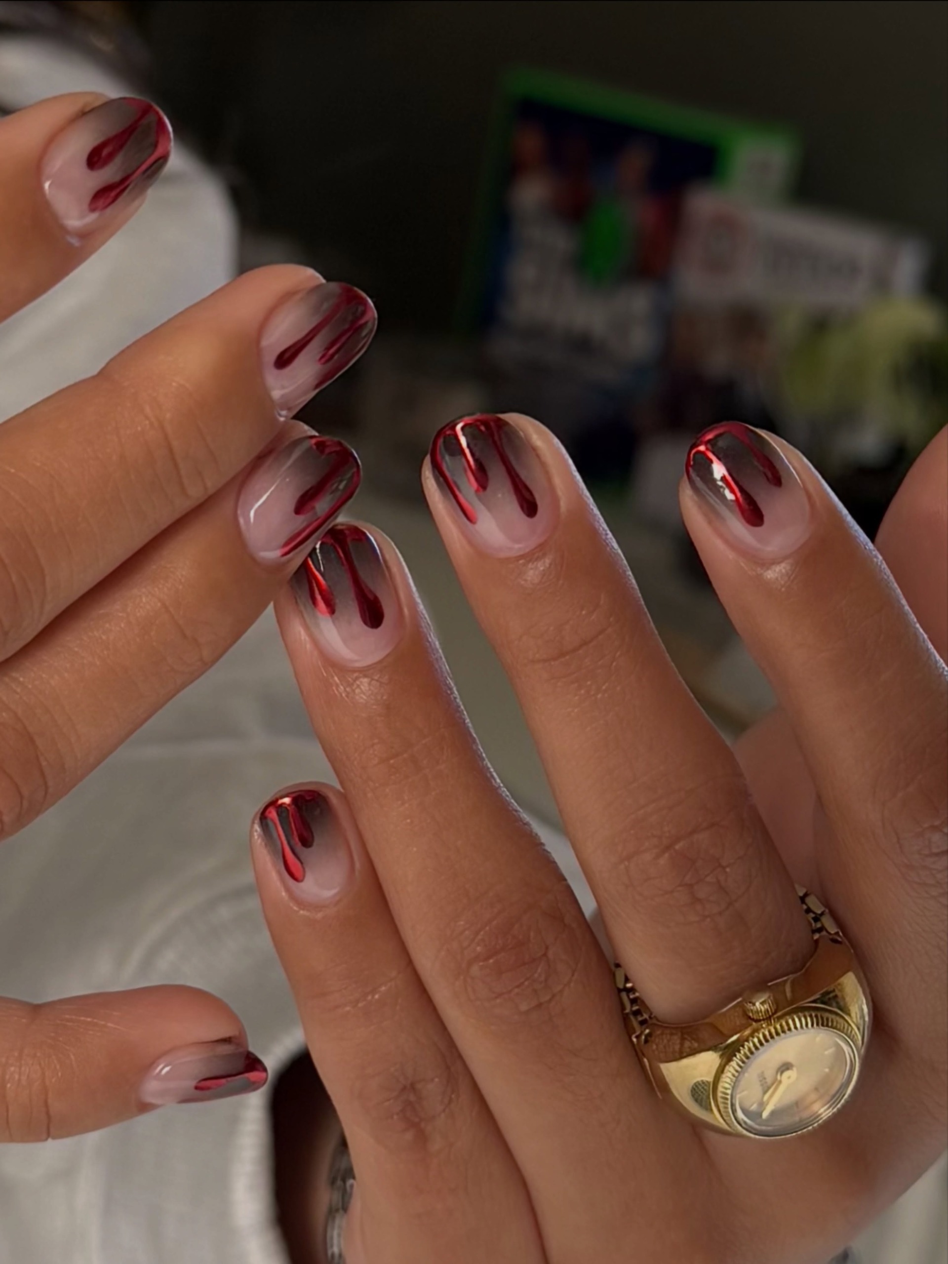 Almond nails with dark red blood drops fading into a sheer pink base, gold rings