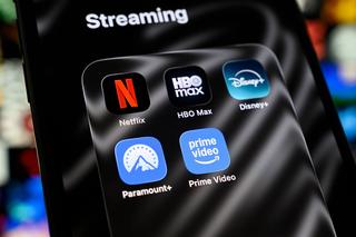 A folder of streaming apps containing Netflix, HBO Max, Disney+, Paramount+, and Prime Video appears on a smartphone screen with a blurred mosaic of streaming content in the background in Creteil, France, on April 17, 2026. The streaming platform released its Q1 2026 results. (Photo by Samuel Boivin/NurPhoto via Getty Images)