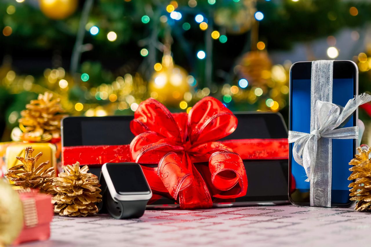 Tablet pc, smartphone and smartwatch with gifts and decorations in front of Christmas tree. Focus on smartphone.