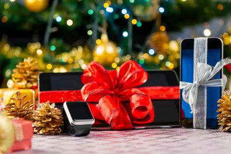 Tablet pc, smartphone and smartwatch with gifts and decorations in front of Christmas tree. Focus on smartphone.