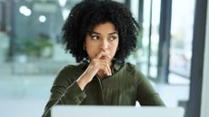 Female office worker in an open plan workspace looking concerned while working on laptop.