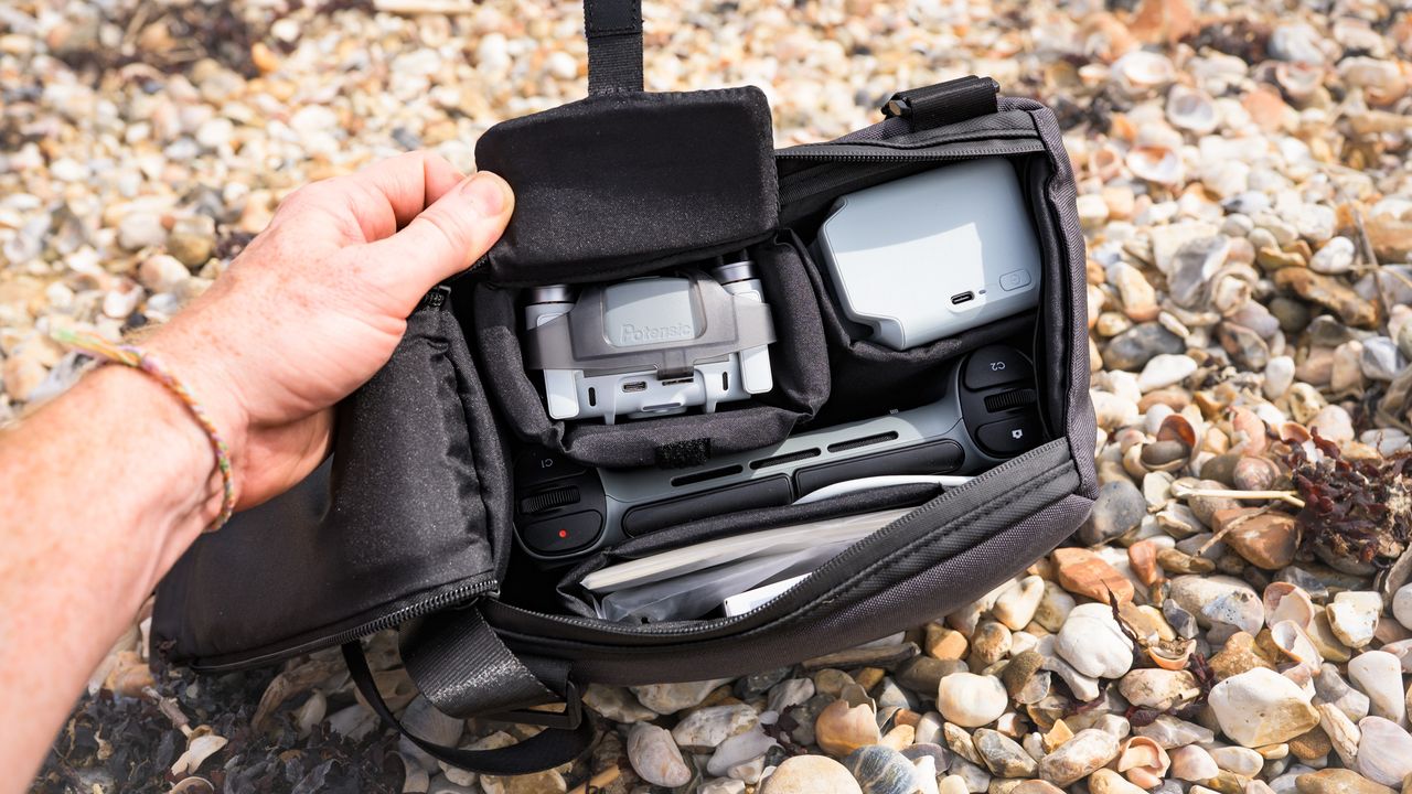 Potensic Atom 3 beginner drone's Fly More Combo bag and its content, on a pebble beach