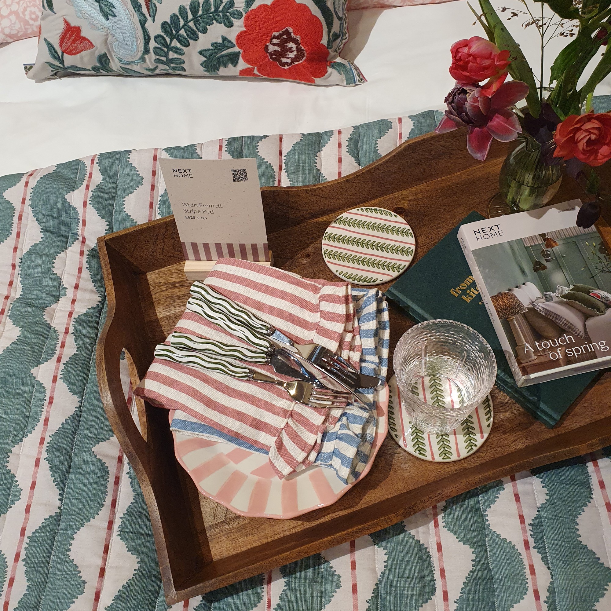 A bed styled with Next's wiggle-print quilt, a floral cushion and a wooden tray to serve breakfast in bed at the launch event for the Decorator range