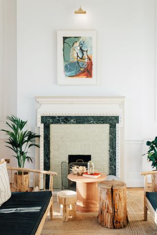 A lounge area with wooden sofas, round wooden coffee tables, round wooden foot stools, a fireplace and potted plants.