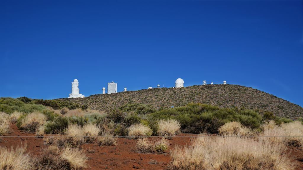 a series of telescopes and white buildings stretch across the desert like mountain landscape with a deep blue sky above.
