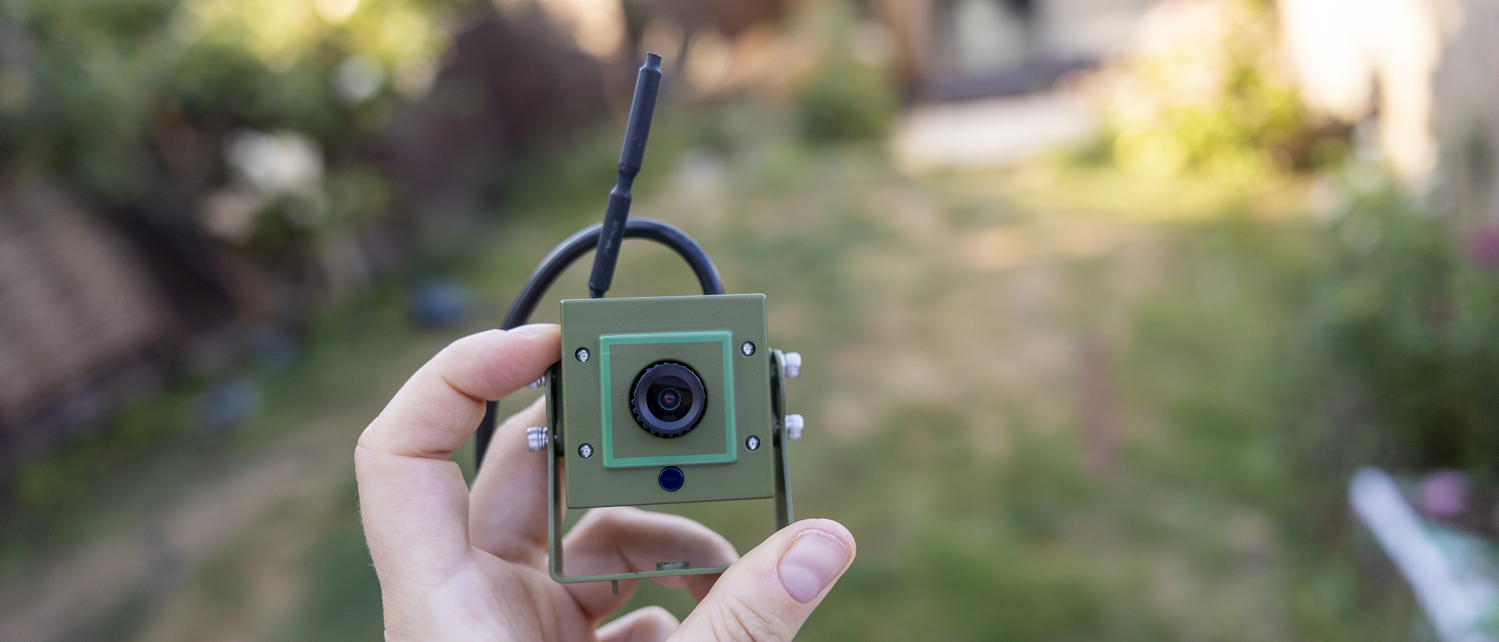 A female hand holding the Green Feathers HD WiFi bird box camera in a summer garden