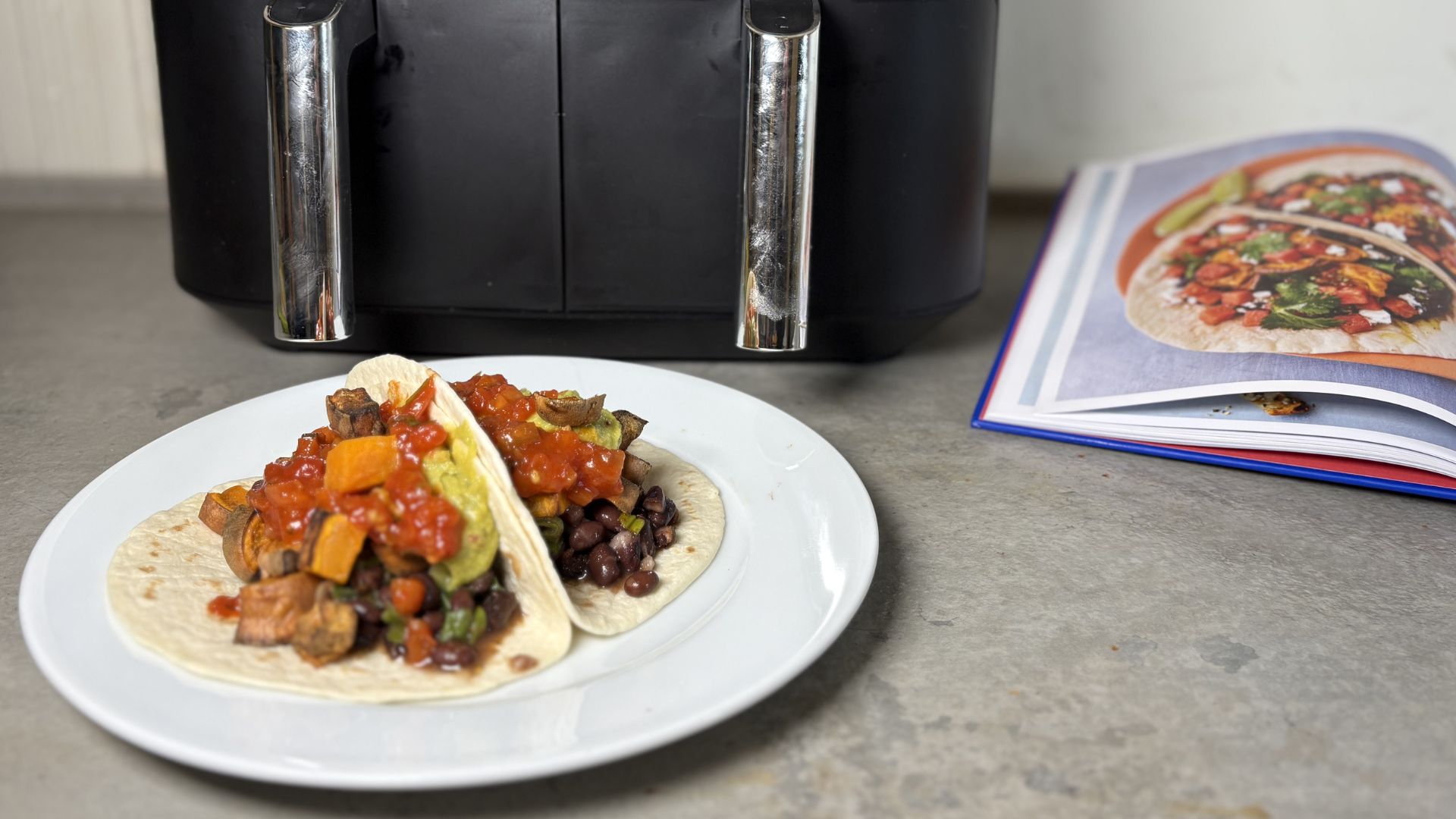 Black bean tortillas in front of an air fryer and an air fryer cookbook, showcasing Jamie Oliver's Air Fryer Hack